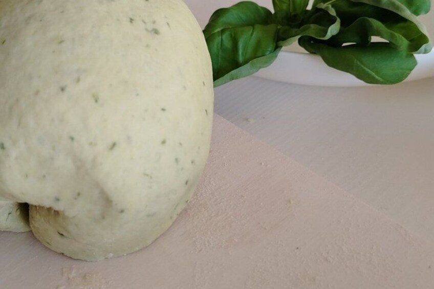 A piece of dough with green herbs on a white surface. 4