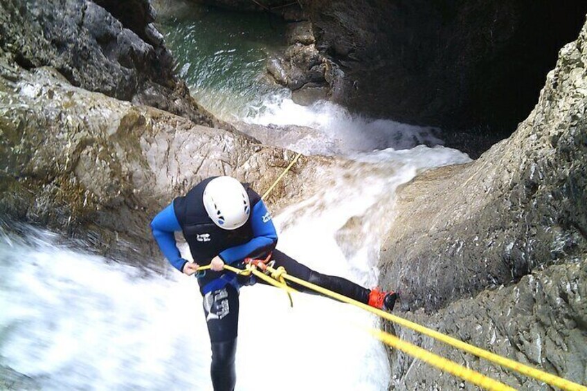 A person rappelling down a rocky cliff with a river below. 5