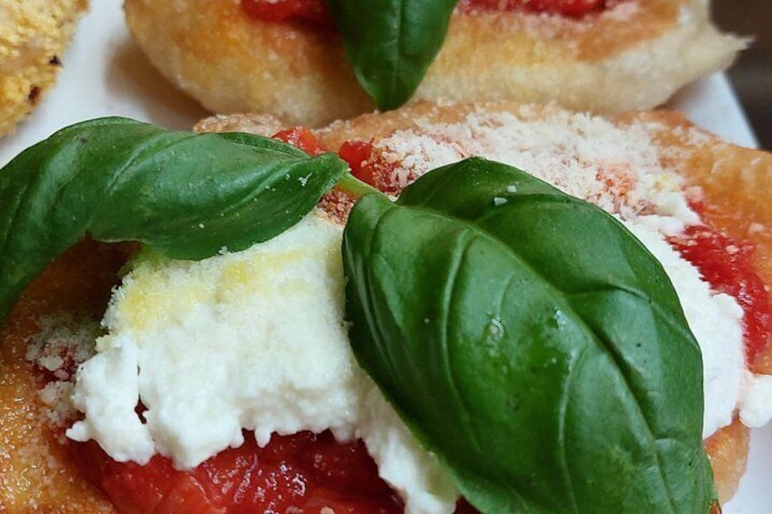A close-up of a food item with a creamy white topping, red sauce, and green basil leaves. 3