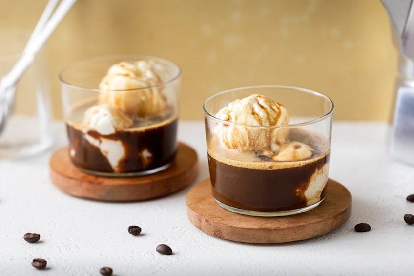 Two glasses of iced coffee with a scoop of ice cream on top, placed on wooden coasters. 2