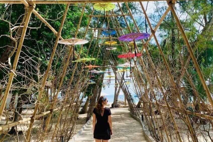 A person walking on a bridge with colorful umbrellas overhead. 1