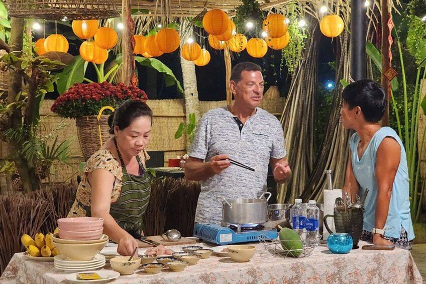 A group of people cooking outdoors with a table set up with cooking utensils and ingredients. 1