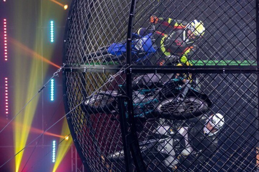 A motorcycle stunt performance inside a cage with bright stage lighting. 3