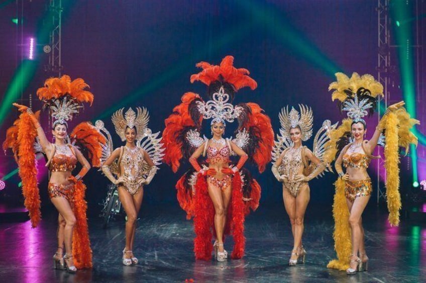 A group of performers in elaborate costumes with feathered headdresses on a stage. 2