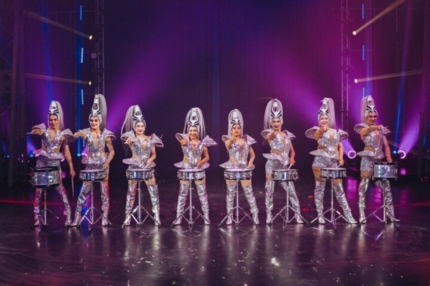 A group of performers in metallic costumes with drums on stage. 5