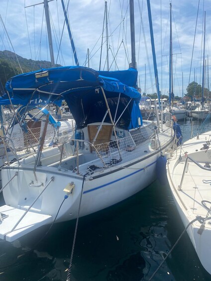 A sailboat docked at a marina with other boats, a blue tarp on the deck, and a mountainous landscape in the background. 5