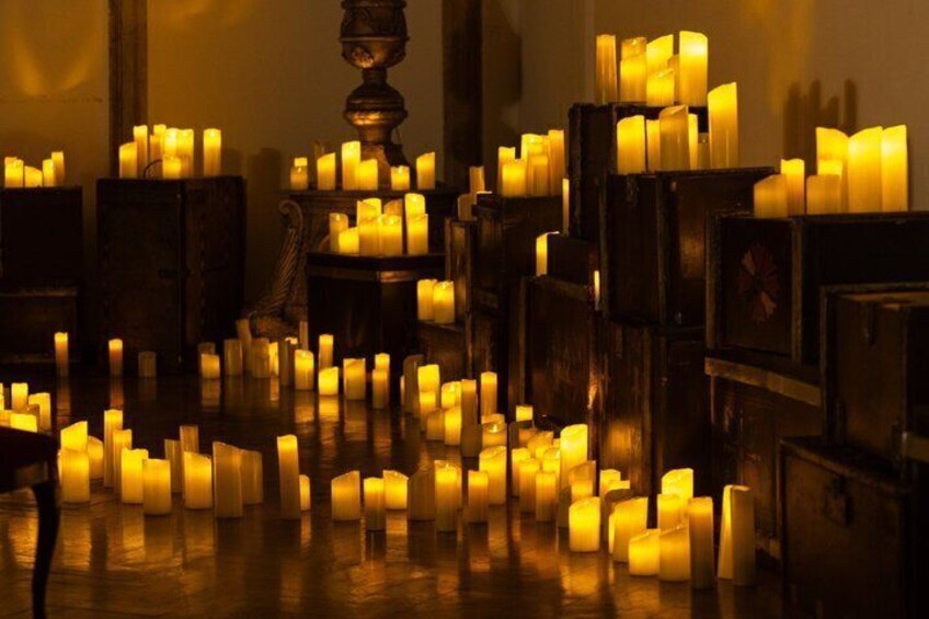 A room with numerous lit candles arranged on tables and shelves. 4