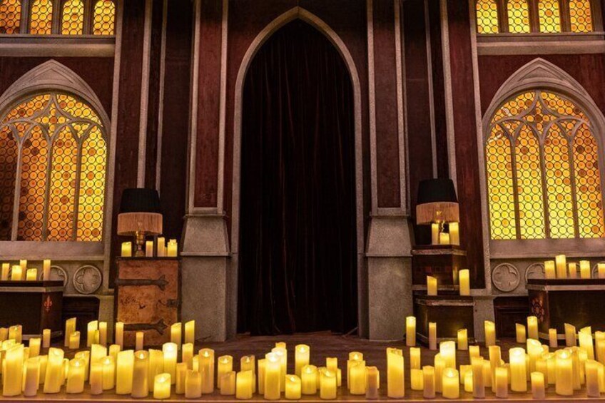 A gothic-style building with stained glass windows, candles, and a dark curtain. 5