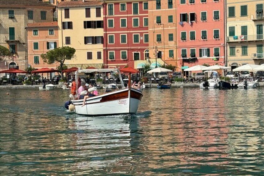 A boat with passengers on a calm waterway, surrounded by colorful buildings and outdoor seating areas. 1
