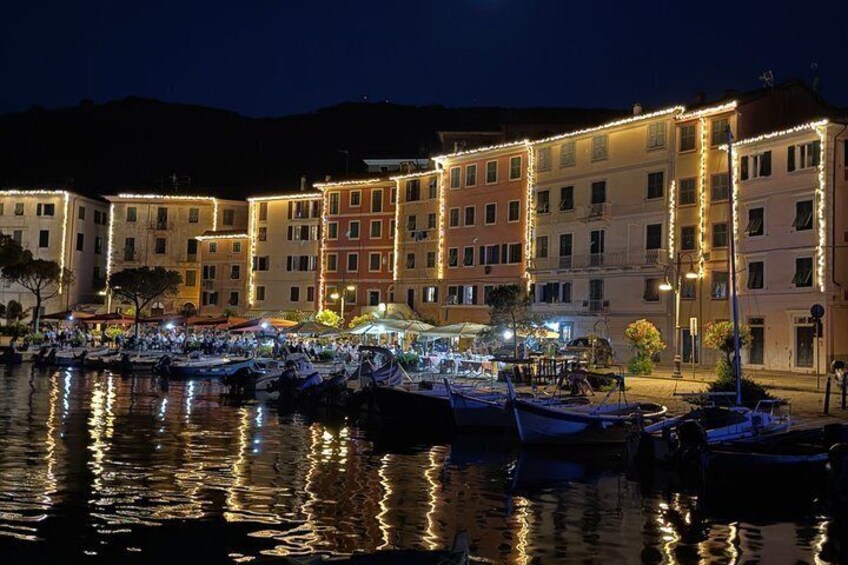 A marina at night with boats docked, illuminated buildings, and a calm waterfront. 2