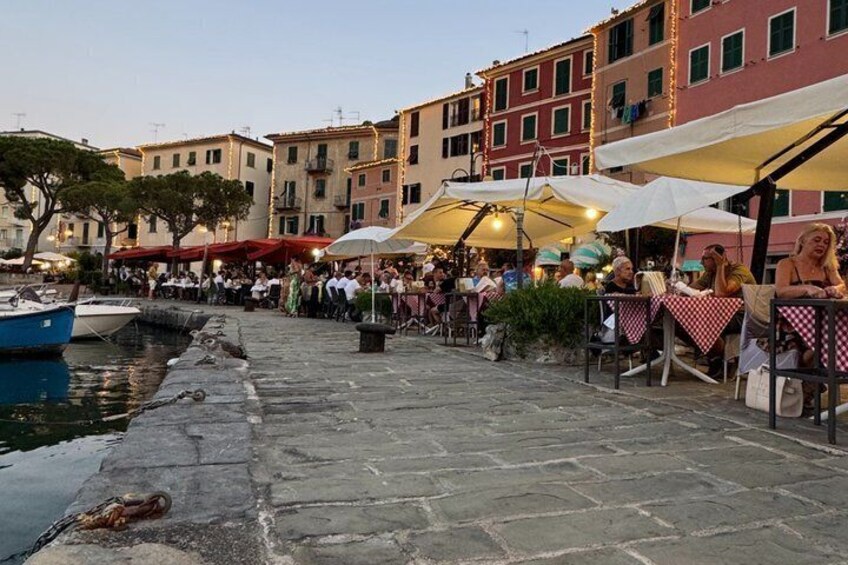 A stone waterfront promenade with outdoor seating, boats, and colorful buildings. 3