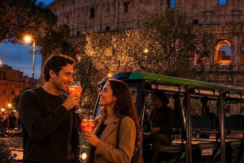 A couple holding drinks in front of a historic building at dusk. 1