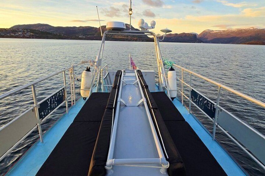A boat deck with a metal railing, a white cabin, and a view of a calm body of water with distant land. 2