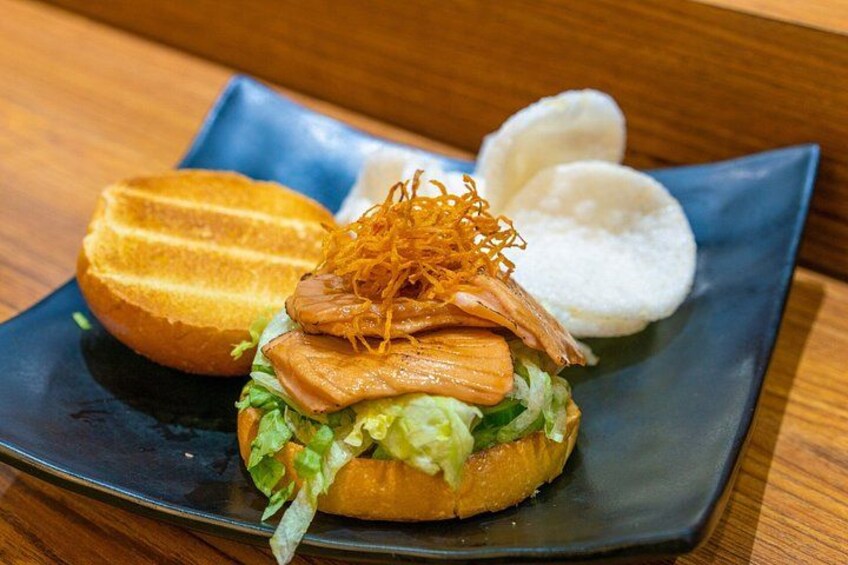 A sandwich with lettuce, a fried item, and a side of white bread and fried onions on a black plate. 5