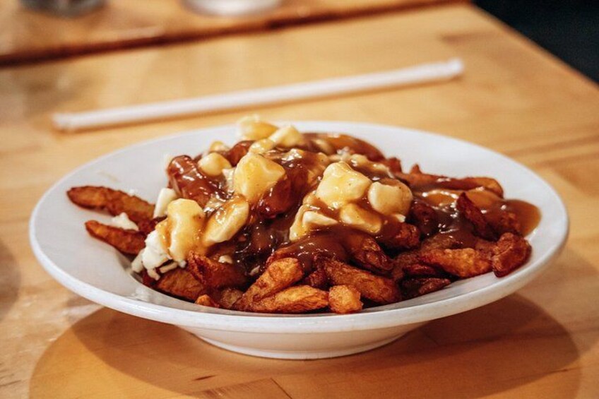 A bowl of poutine with fries, cheese curds, and gravy. 2