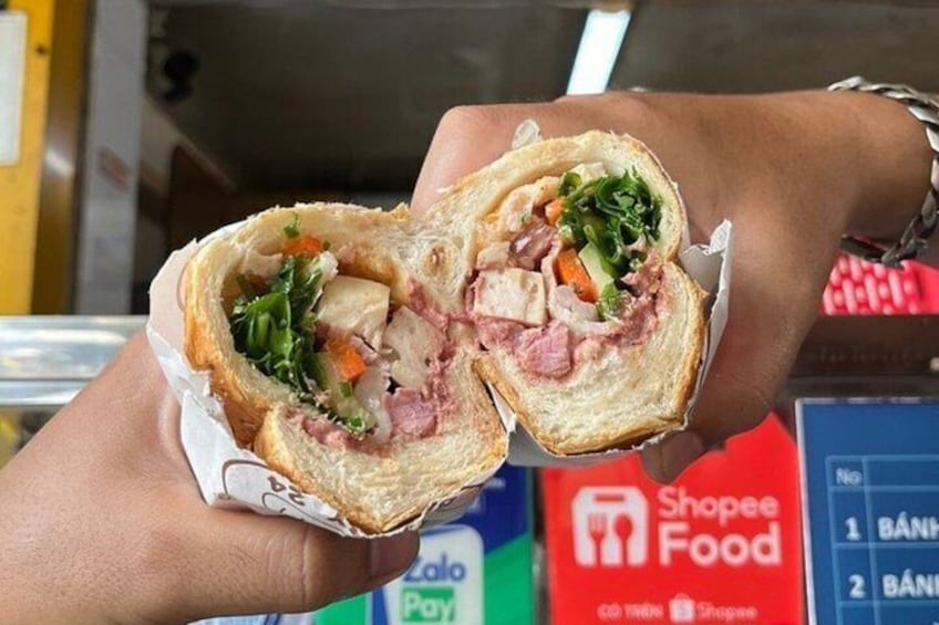 A person holding a half-eaten sandwich with visible lettuce, meat, and bread. 3