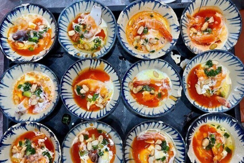 A tray of seafood dishes with a red sauce, garnished with herbs and nuts. 4