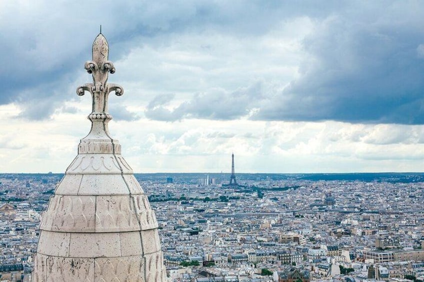 A domed structure with a fleur-de-lis atop, overlooking a cityscape with the Eiffel Tower in the distance. 3