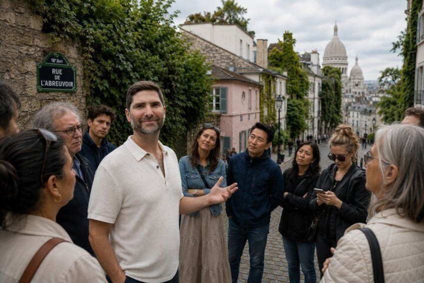 A group of people standing on a cobblestone street with a sign reading 'RUE DE L'ABREUVIOIR' and a dome in the background. 1