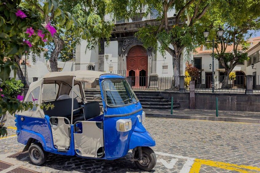 A blue three-wheeled vehicle parked on a cobblestone street with a building in the background. 5