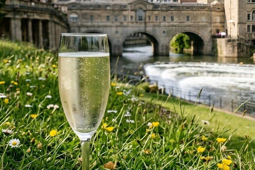 A glass of champagne on grass with a river and a bridge in the background. 5