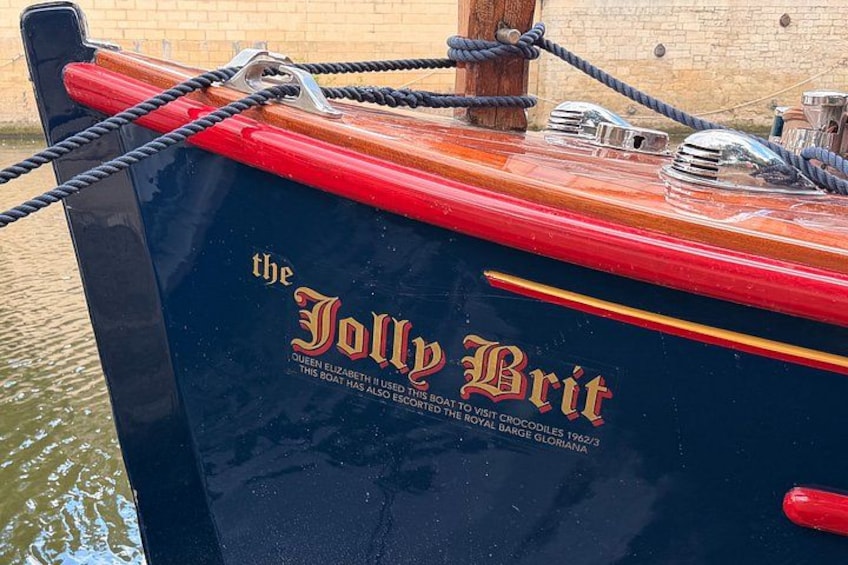 A boat named 'the Jolly Brit' with a red and black hull, tied to a dock with ropes. 4