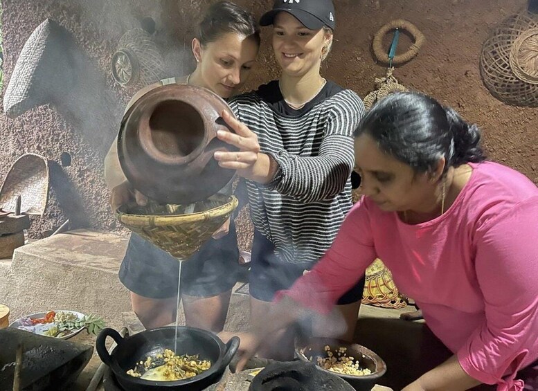 Three people cooking outdoors with clay pots and a traditional stove. 2