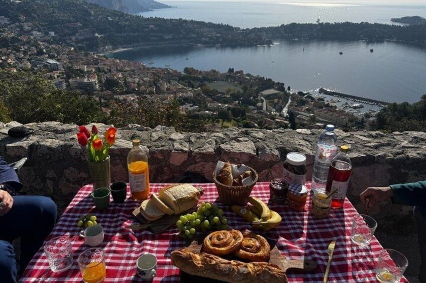 A picnic table with food and drinks overlooking a coastal town. 1