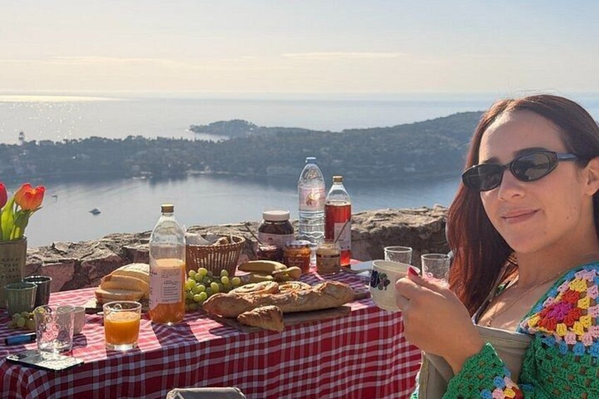 A picnic setup with food and drinks on a table overlooking a coastal landscape. 2