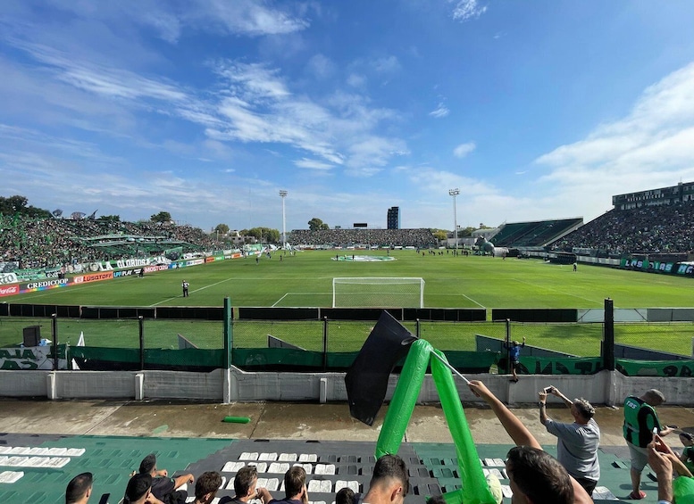A football stadium with green seating, a goalpost, and advertisements on the sidelines. 1