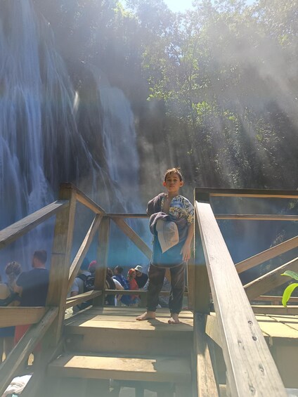 A person standing on a wooden platform with a waterfall in the background. 3
