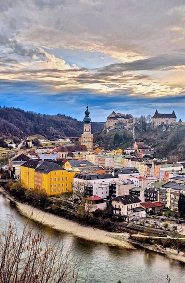 A town with colorful buildings, a river, and a castle on a hill. 1