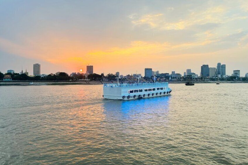 A riverboat on a calm river with a city skyline in the background during sunset. 2