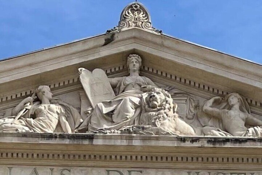 A classical building facade with a central sculpture of a seated figure holding a scroll, flanked by two lions and two reclining figures. 4