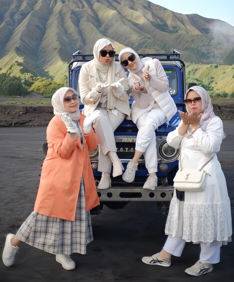 Four people posing in front of a vehicle with a mountainous backdrop. 3