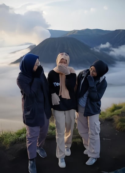 Three people standing on a path with a mountainous landscape in the background. 2