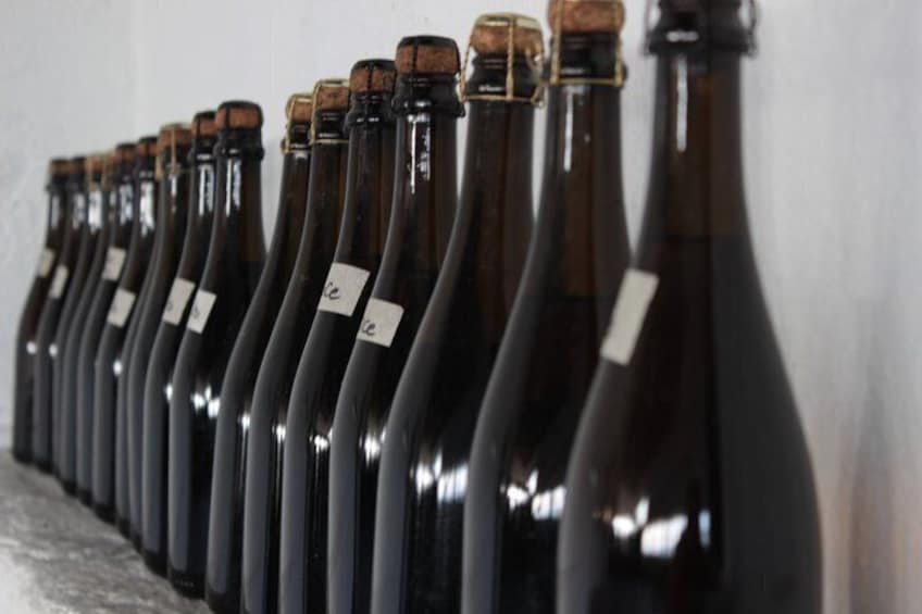 A row of dark glass bottles with corks, lined up against a wall. 2