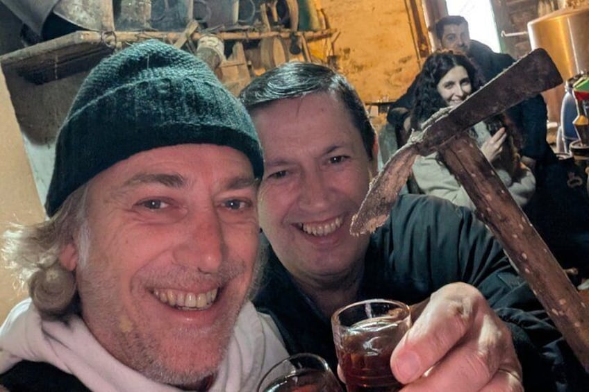Two people holding a hammer and a glass of liquid, with a rustic background. 5