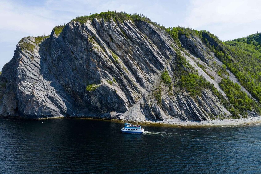 A boat on a calm body of water with a large rocky cliff in the background. 5