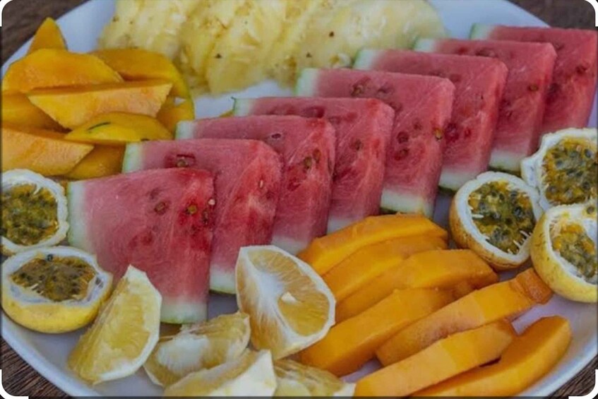 A plate of sliced fruits including watermelon, passion fruit, mango, and papaya. 3