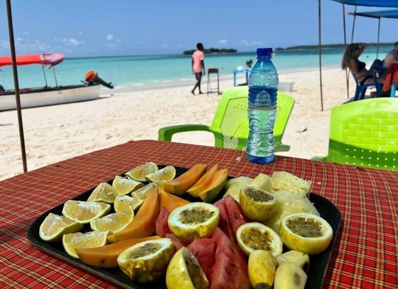 A beach scene with a table displaying sliced fruits and a water bottle. 5