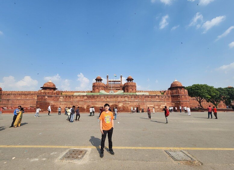 A large, historic fort with red walls and domed towers, surrounded by a paved area with people walking. 2