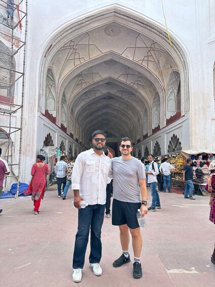 Two men standing in front of a large, ornate building with a high ceiling and intricate architectural details. 3