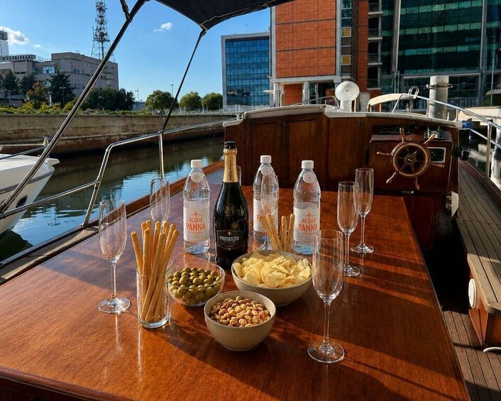 A boat deck with bottles of Prosecco, glasses, snacks, and a wooden table. 2