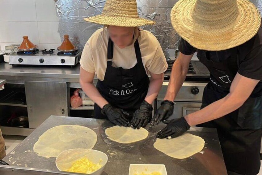 Two people preparing food, one wearing a straw hat, on a kitchen counter with dough and a bowl of eggs. 4