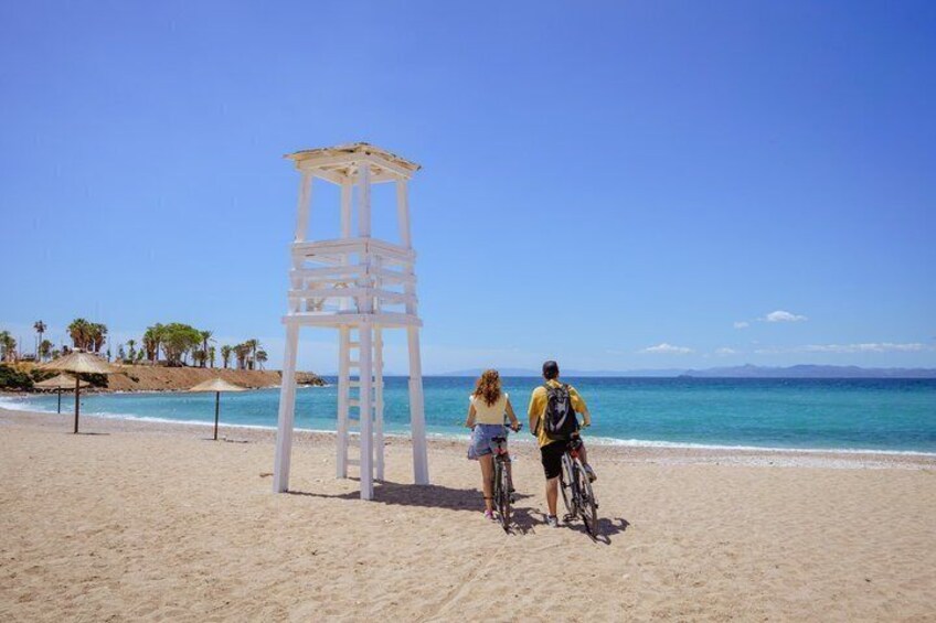 A beach with a white lifeguard tower, two people on bicycles, and a clear blue sky. 2