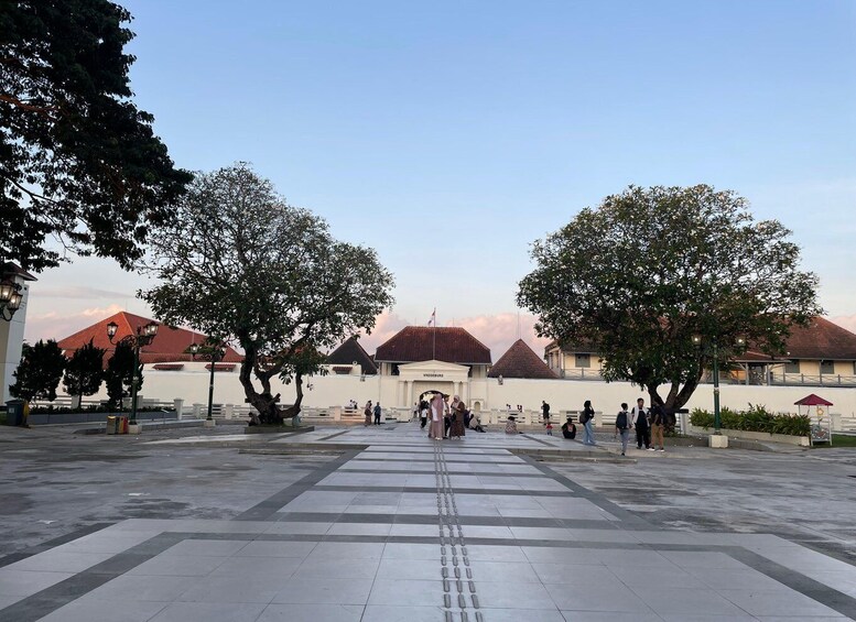A plaza with tiled flooring, two large trees, and buildings with red roofs in the background. 3