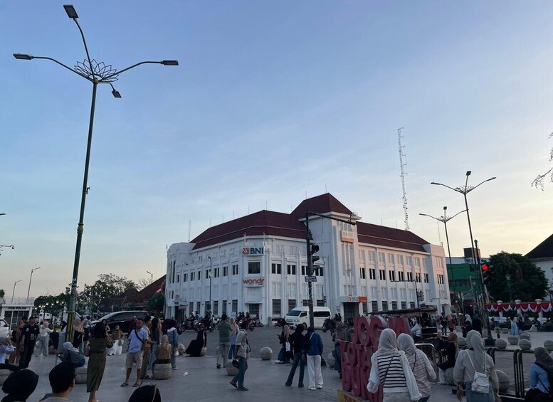 A busy urban square with a prominent white building labeled 'BNI' and a clear blue sky. 4