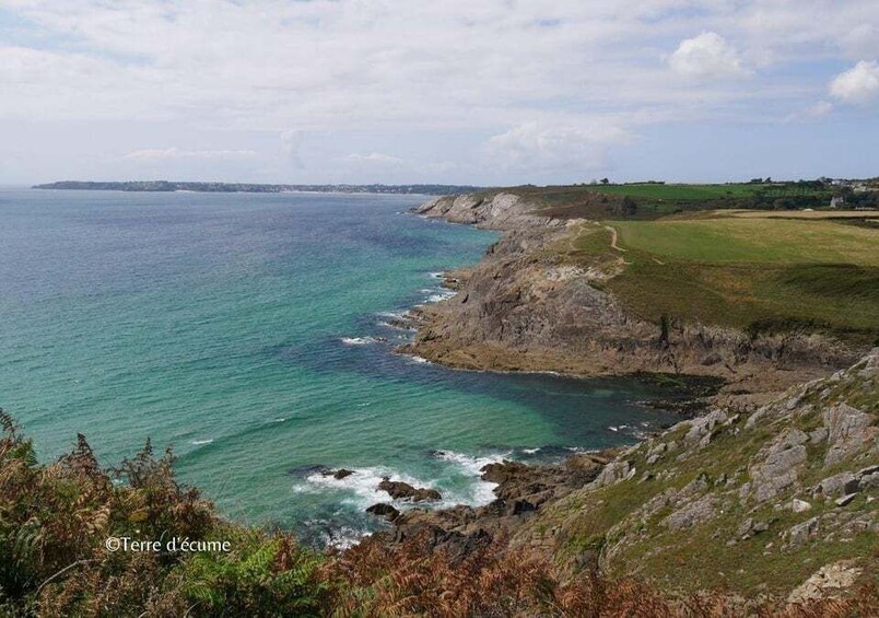 A coastal landscape with a rocky shoreline, clear blue sea, and distant land. 4