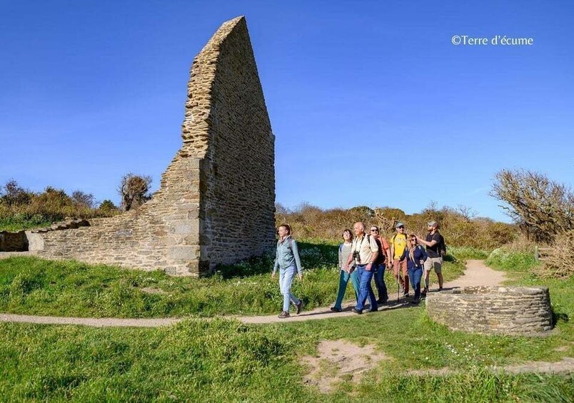 A group of people walking along a path beside a stone structure. 1